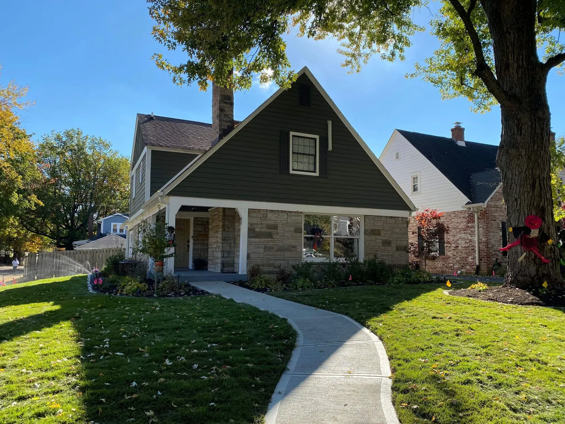 Suburban house with stone facade, dark roof, and curved walkway in a sunny yard