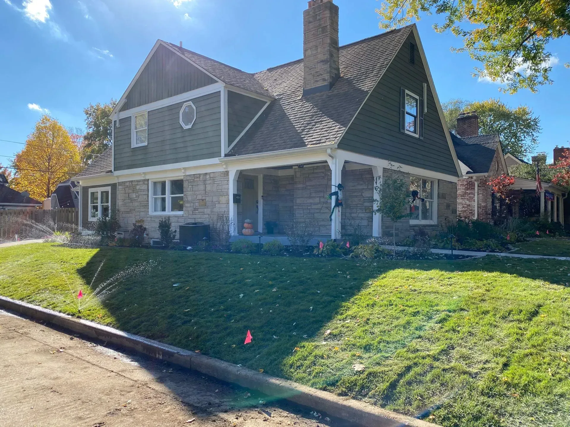 Suburban house with stone porch, steep roof, and a grassy front yard in bright sunlight