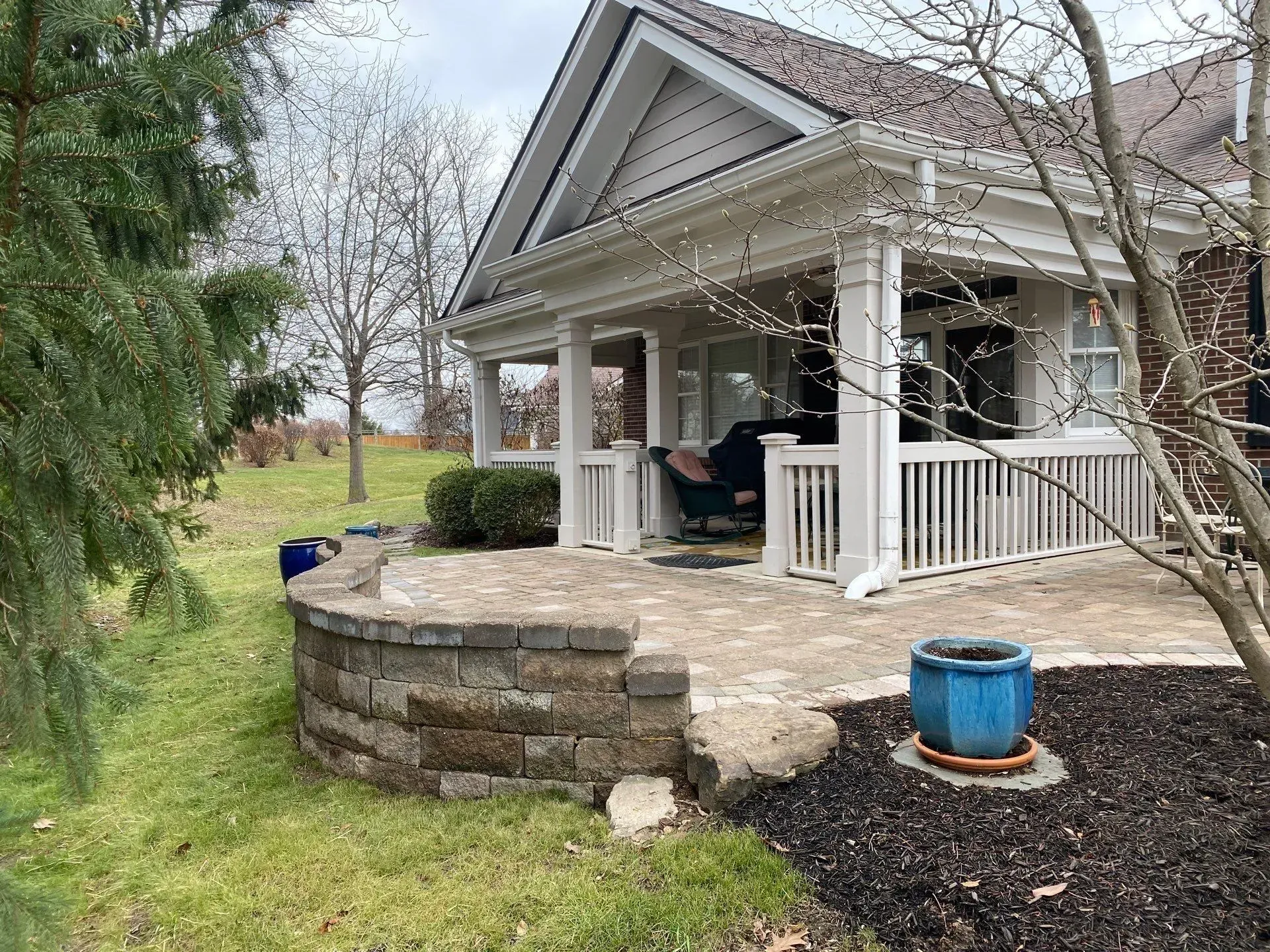 House porch with stone retaining wall, white railings, and blue planter in a landscaped yard