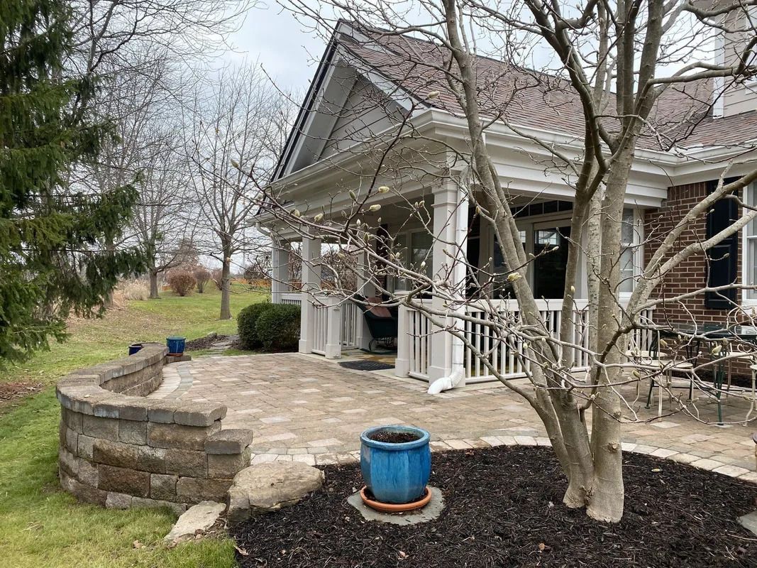 Brick house porch with white railings, stone patio, and leafless trees in a yard