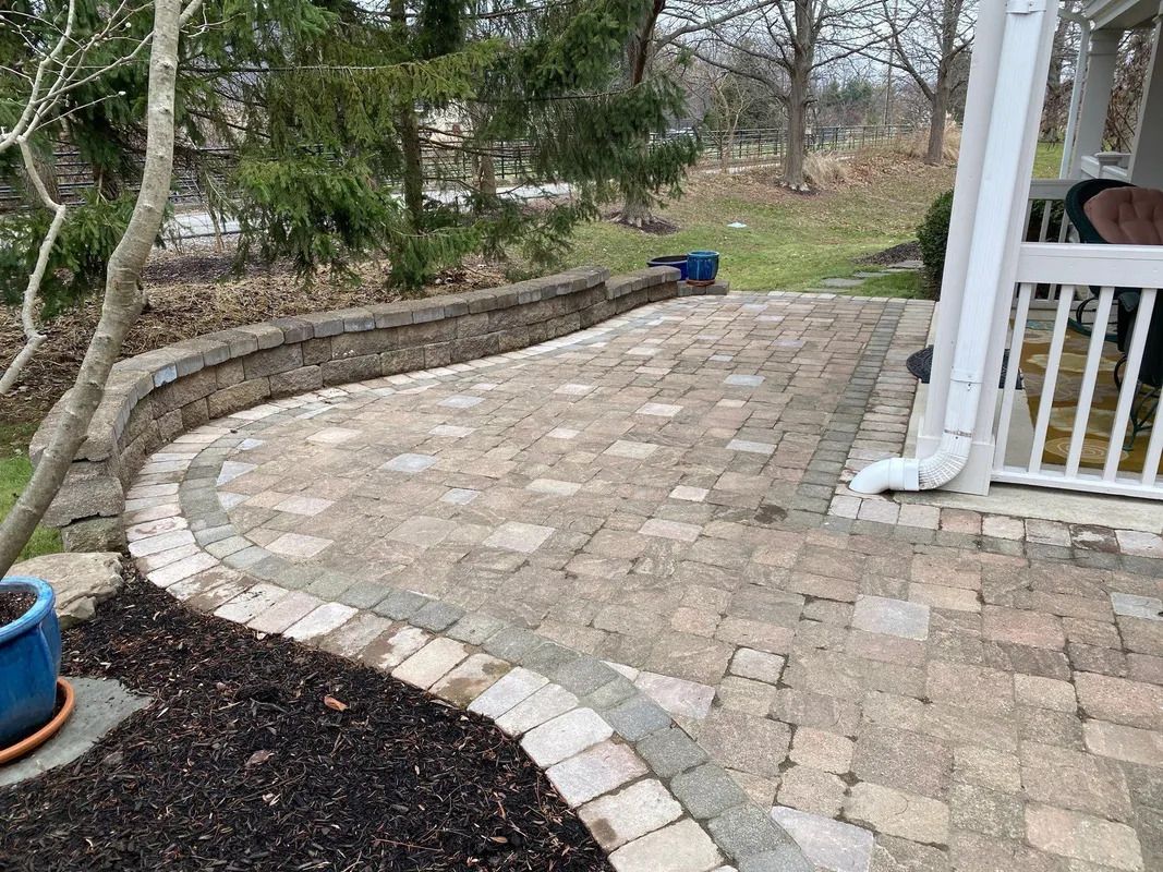 Stone patio walkway beside garden beds and a porch railing in a yard