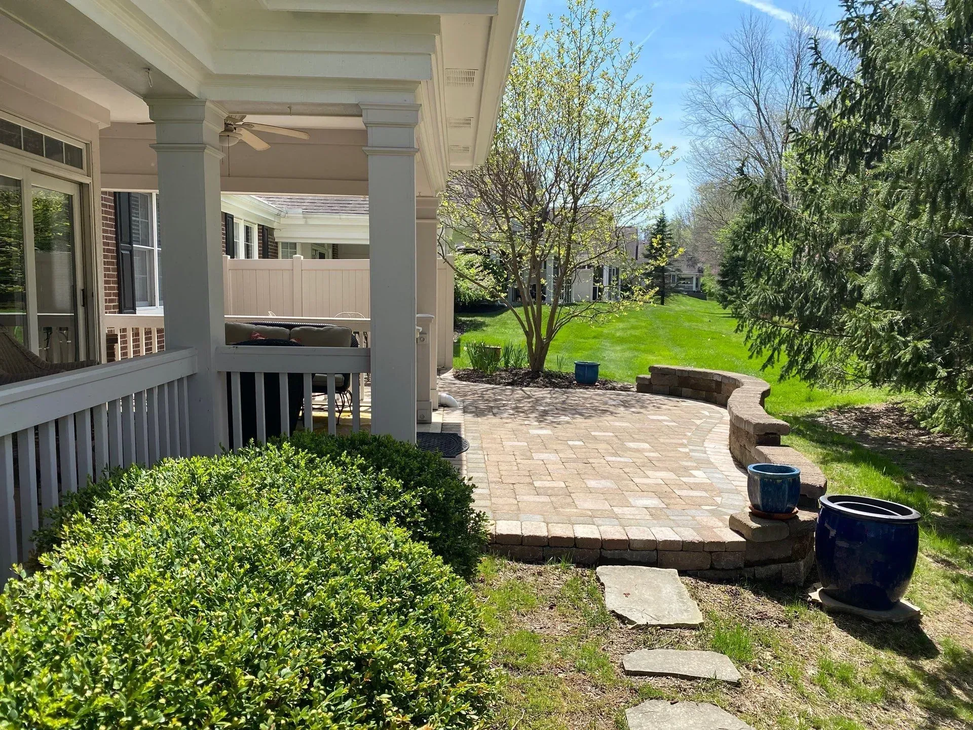 Front porch beside a stone patio, with green lawn, shrubs, and a sunny backyard view
