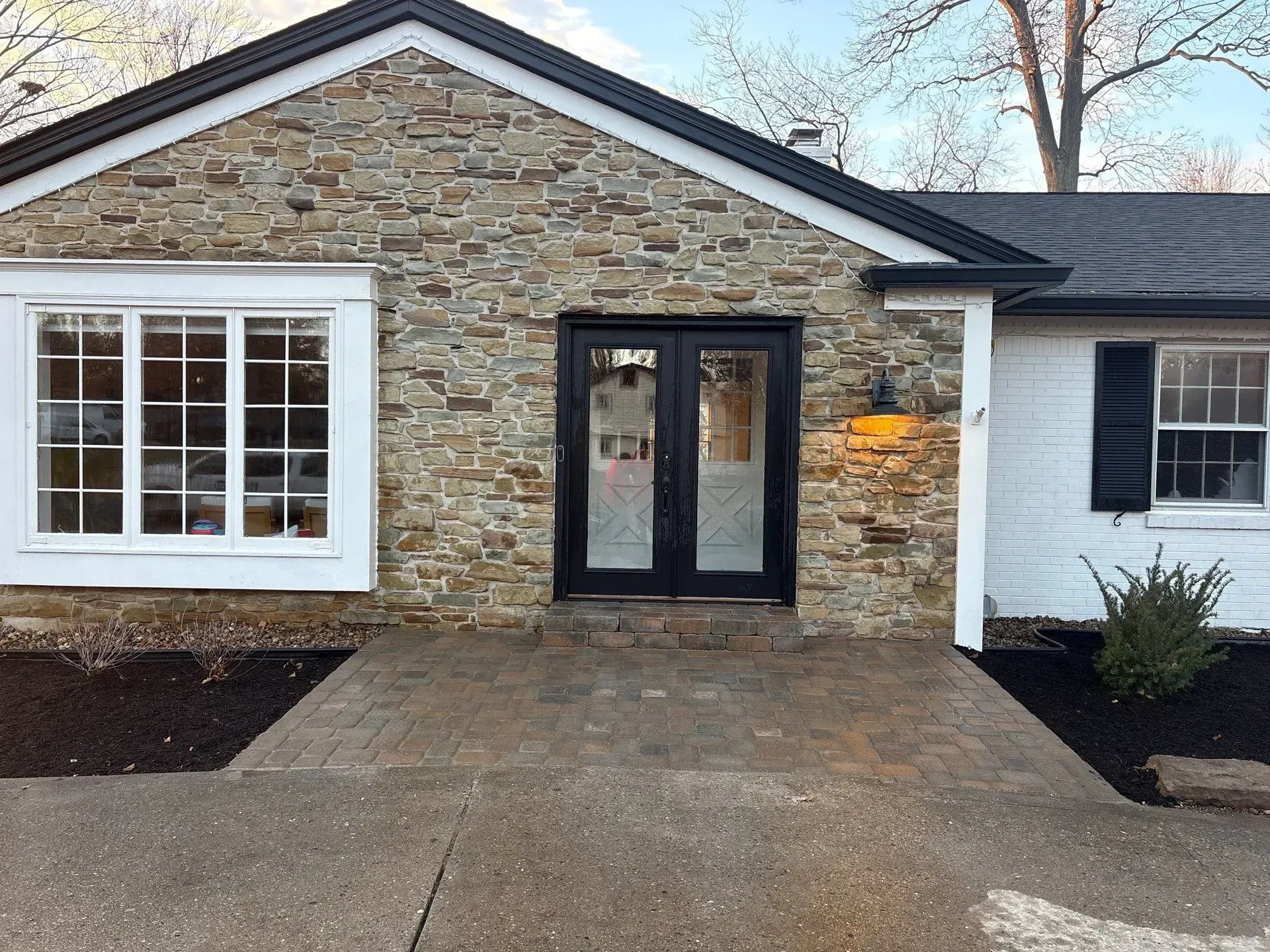 Stone house front entry with white-trimmed windows and dark double doors