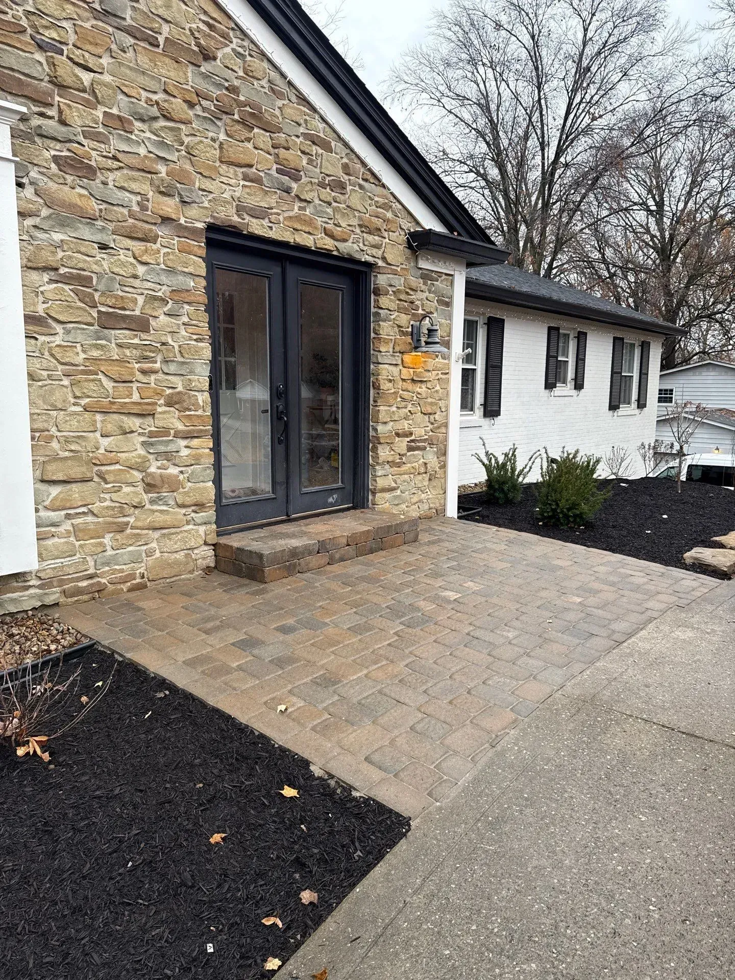Stone house entry with double doors, paver walkway, and landscaped mulch beds