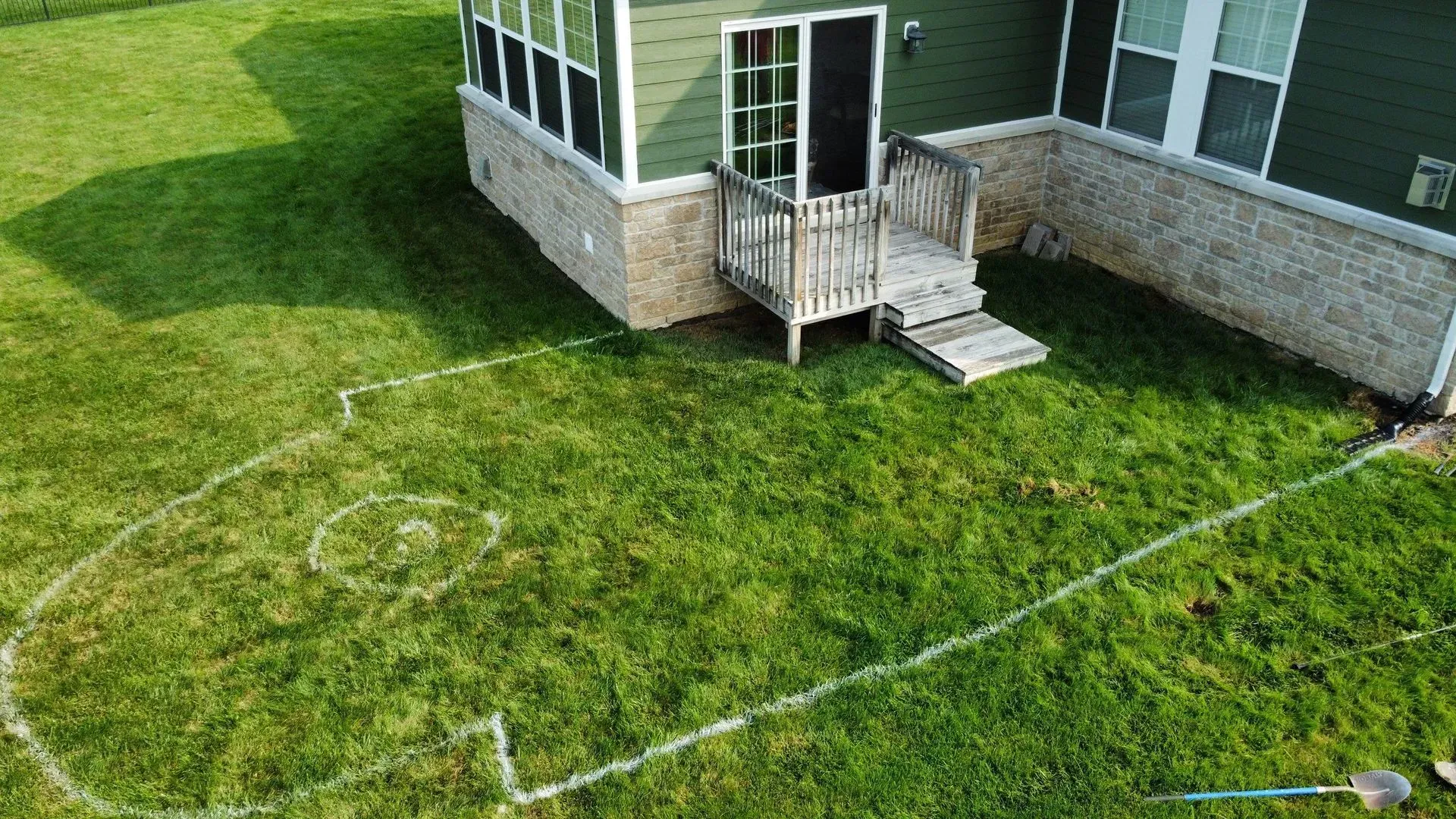 Backyard lawn with white hose lines near a house porch and stone foundation