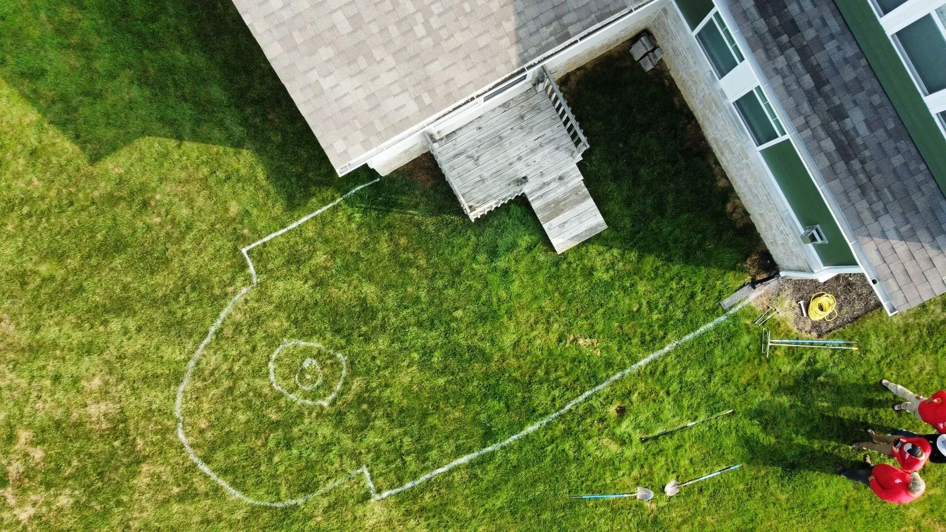 Aerial view of a house corner, lawn, and a white boundary line marking a yard area.
