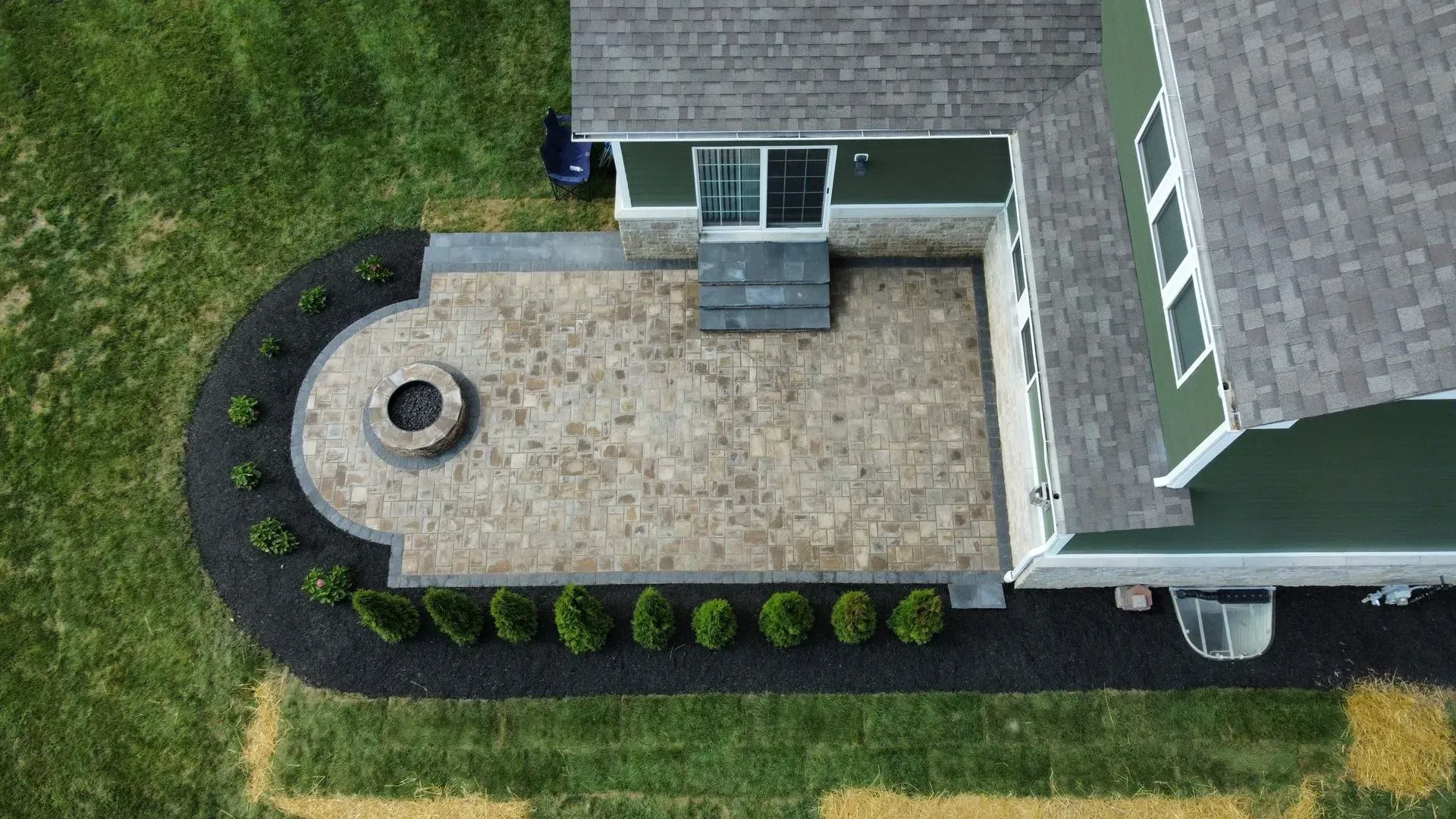 Aerial view of a house patio with stone pavers, circular fire pit, and landscaped edging