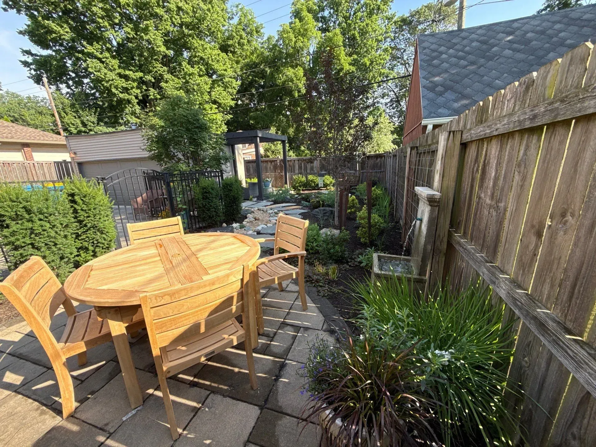 Wooden patio table and chairs on a sunny backyard deck beside a fence and garden plants