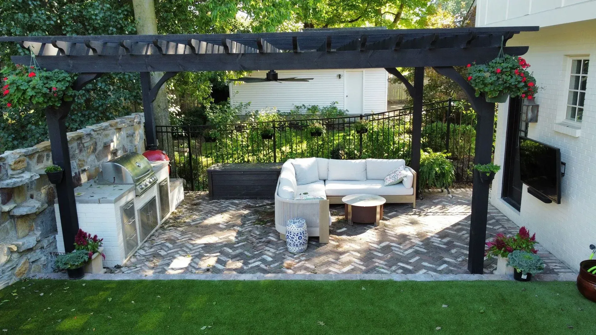 Backyard pergola with white outdoor sofa, coffee table, and potted plants over a stone patio