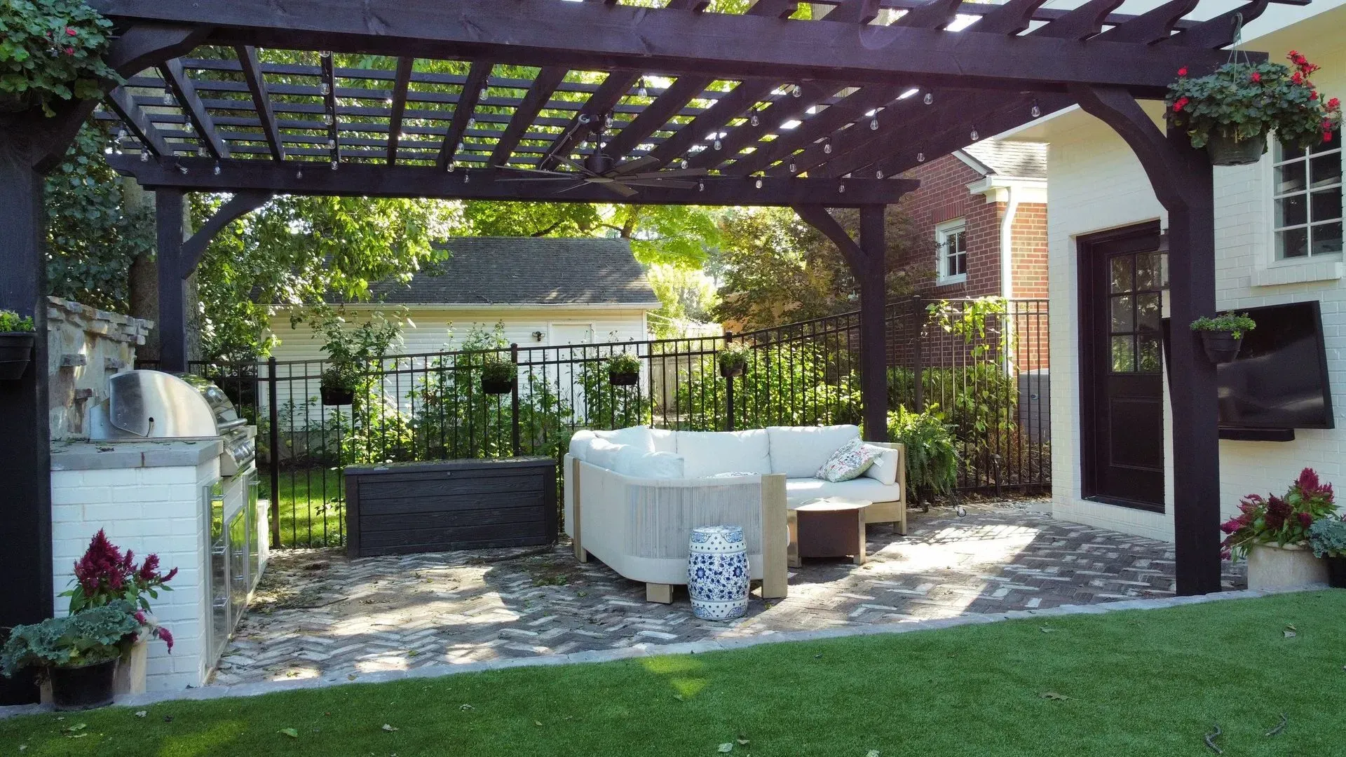 Backyard patio with a wooden pergola, stone paving, outdoor seating, and a small lawn in the foreground