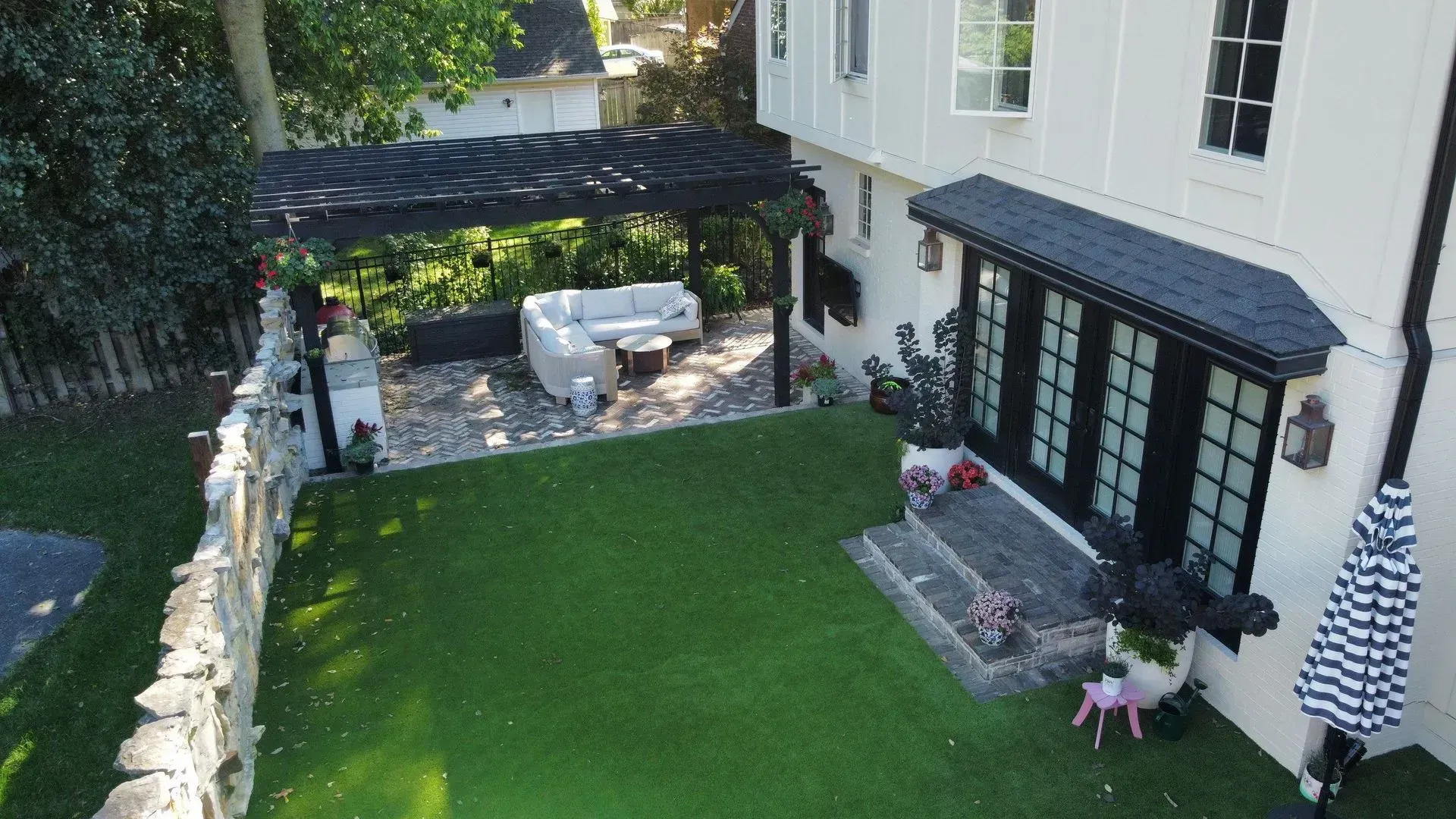 Backyard patio with pergola, white house exterior, lawn, and two people near the steps