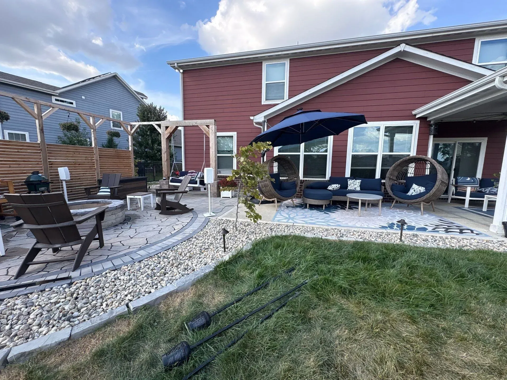 Backyard patio with stone seating area, red house, umbrella, fire pit, and hanging chair