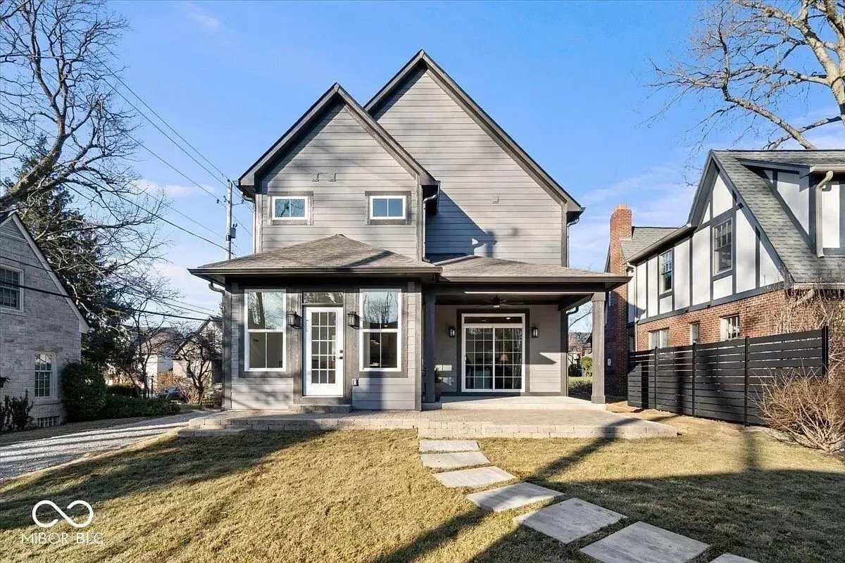 Two-story beige house with a covered porch, front lawn, and stone walkway on a sunny day