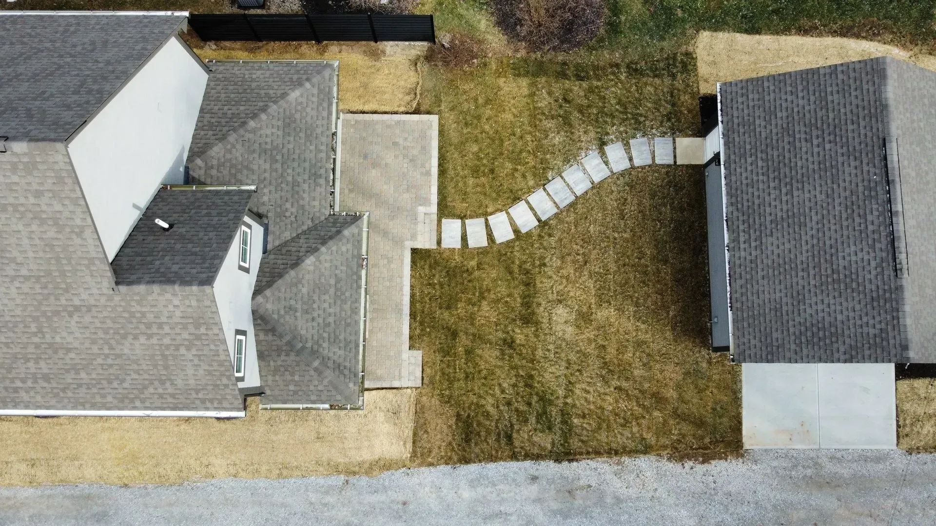 Aerial view of two gray-roofed houses with a curved stepping-stone path across a grassy yard.