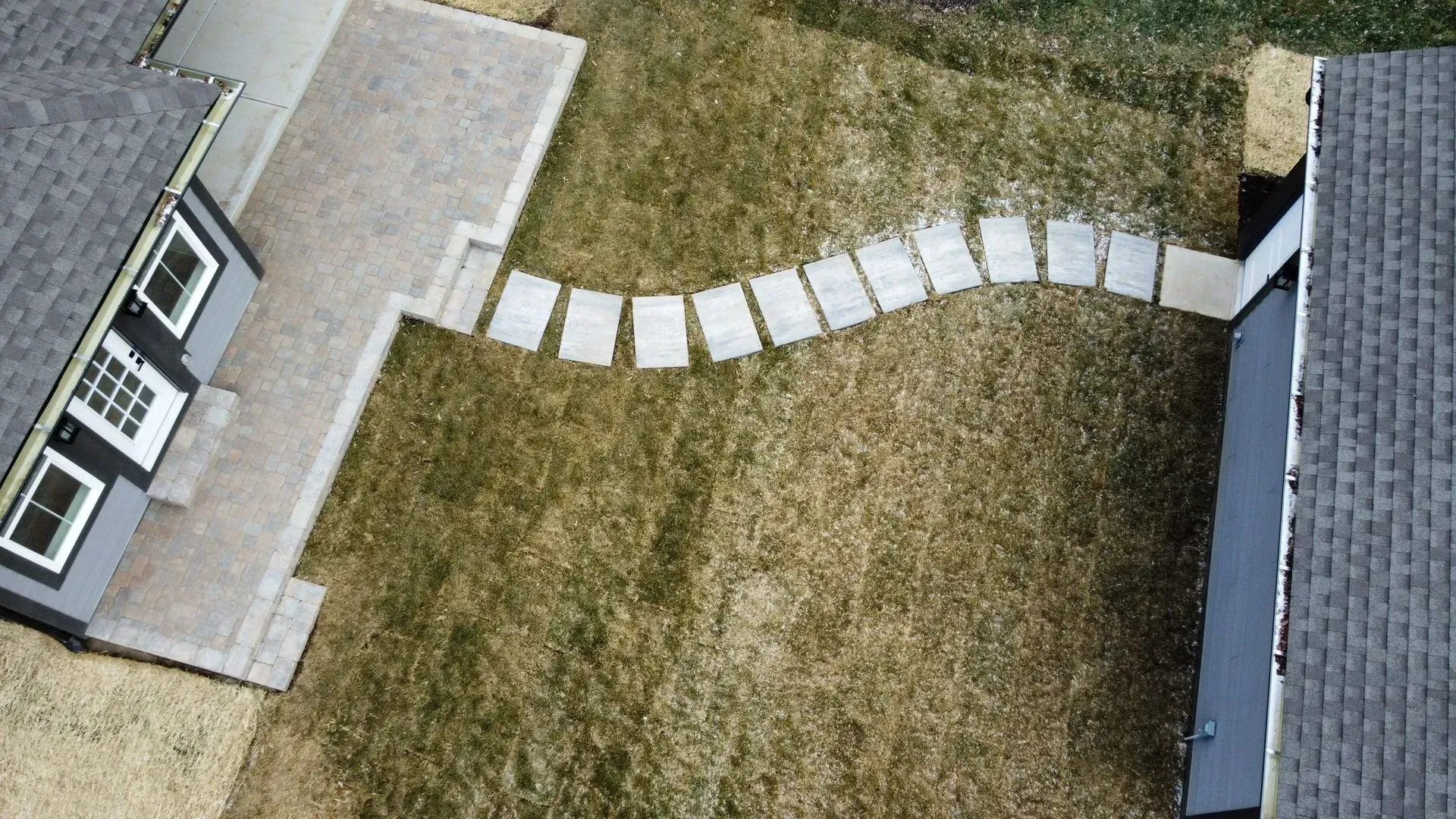 Aerial view of a backyard with a curved stone walkway between a house and a garage.