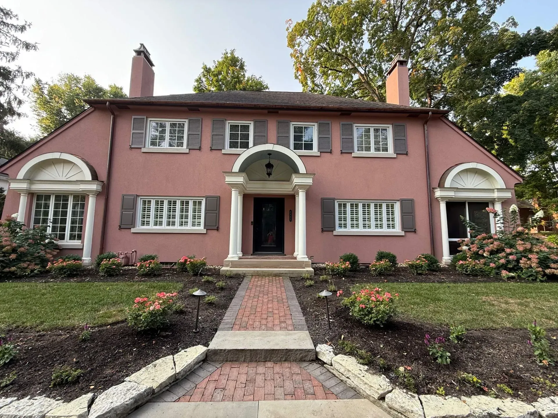 Front view of a pink two-story house with white trim and a brick path through a landscaped garden