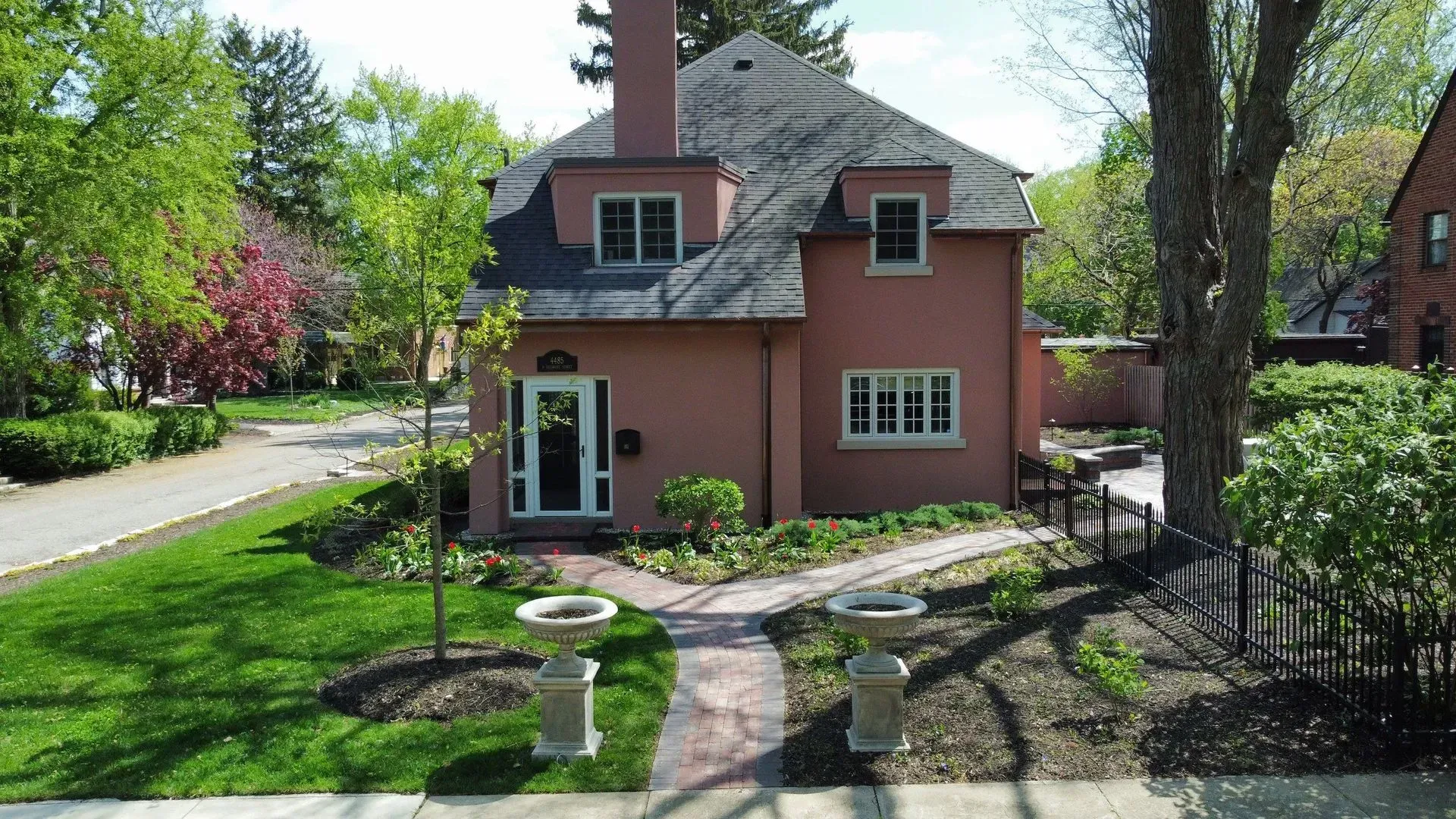 Small pink house with a garden path, trees, and a sunlit front yard