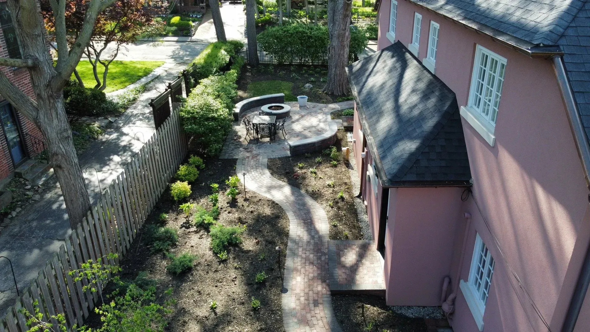 Aerial view of a pink house beside a stone garden path with trees and a circular patio.