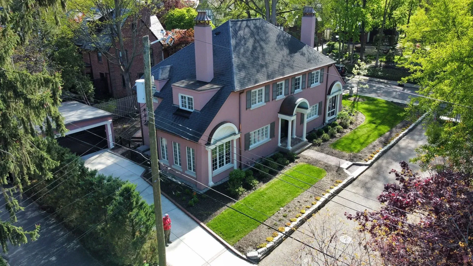 Aerial view of a pink brick house with a gray roof, front lawn, and tree-lined street.