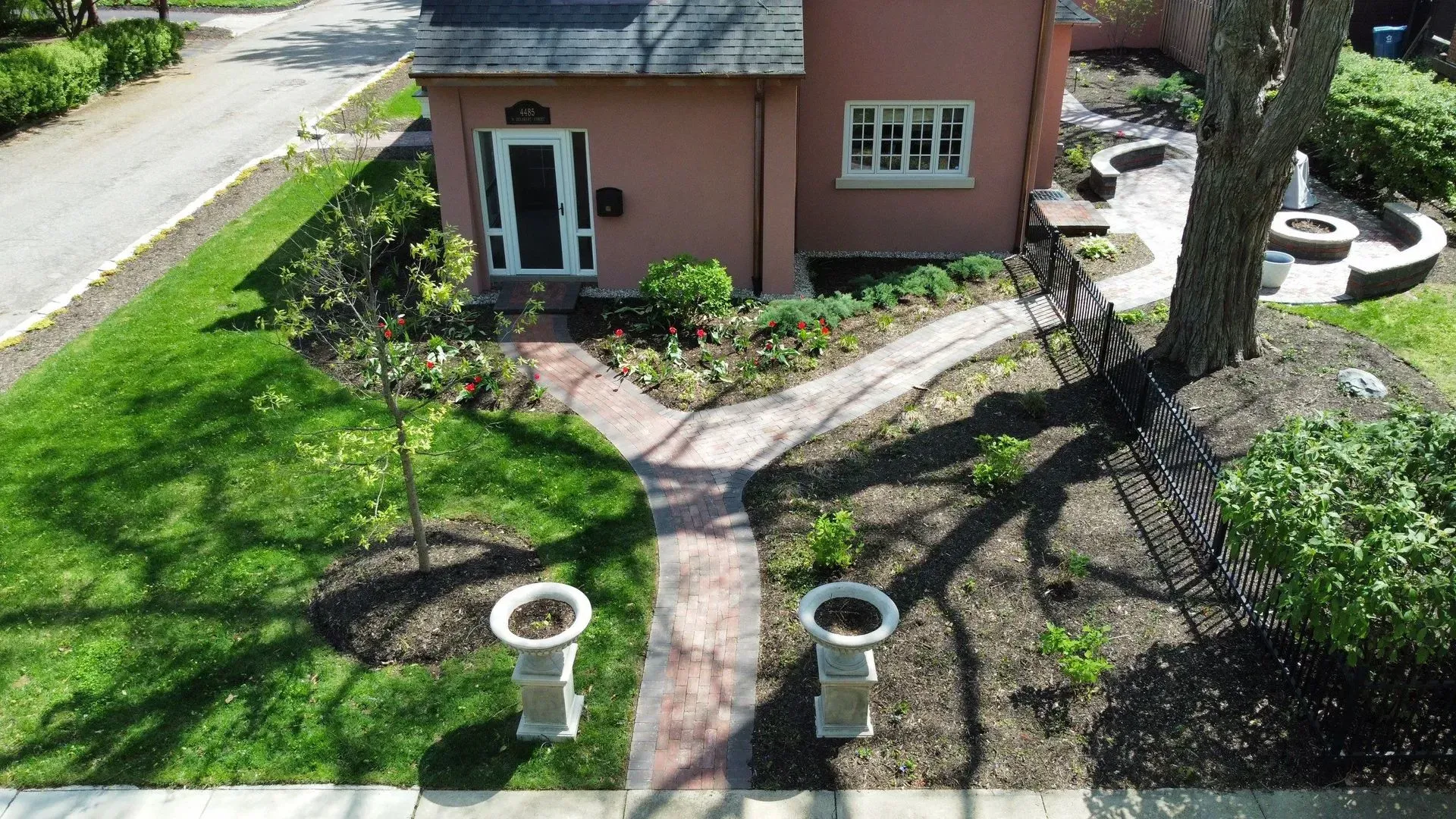 Aerial view of a pink house with a curved stone path, green lawn, and circular planters by the entrance