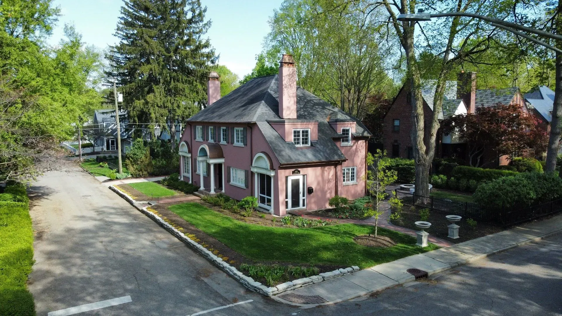 Brick house on a tree-lined residential street beside a curved road and sidewalk