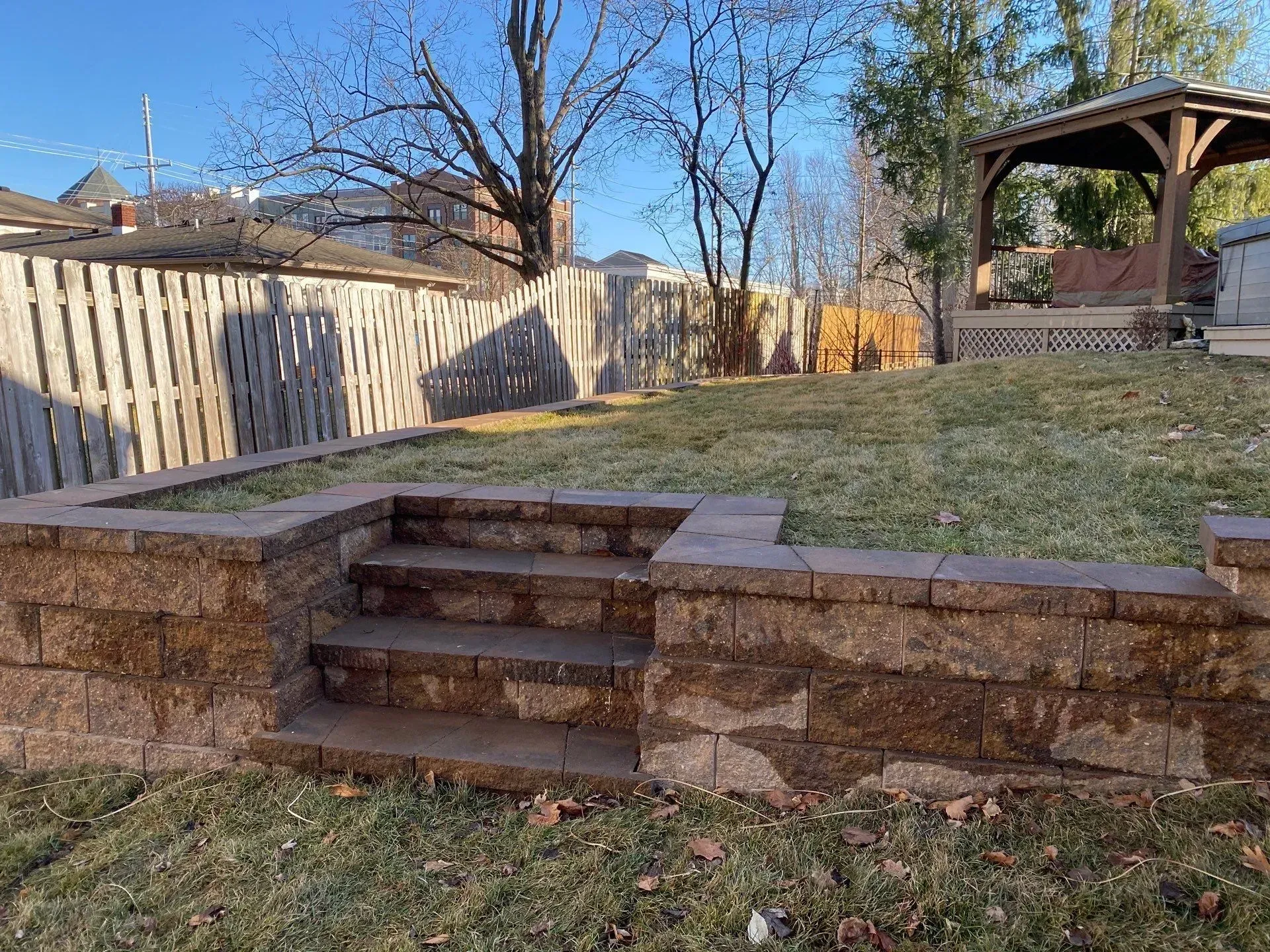 Backyard stone steps leading to a grassy yard with a gazebo and wooden fence under a clear blue sky
