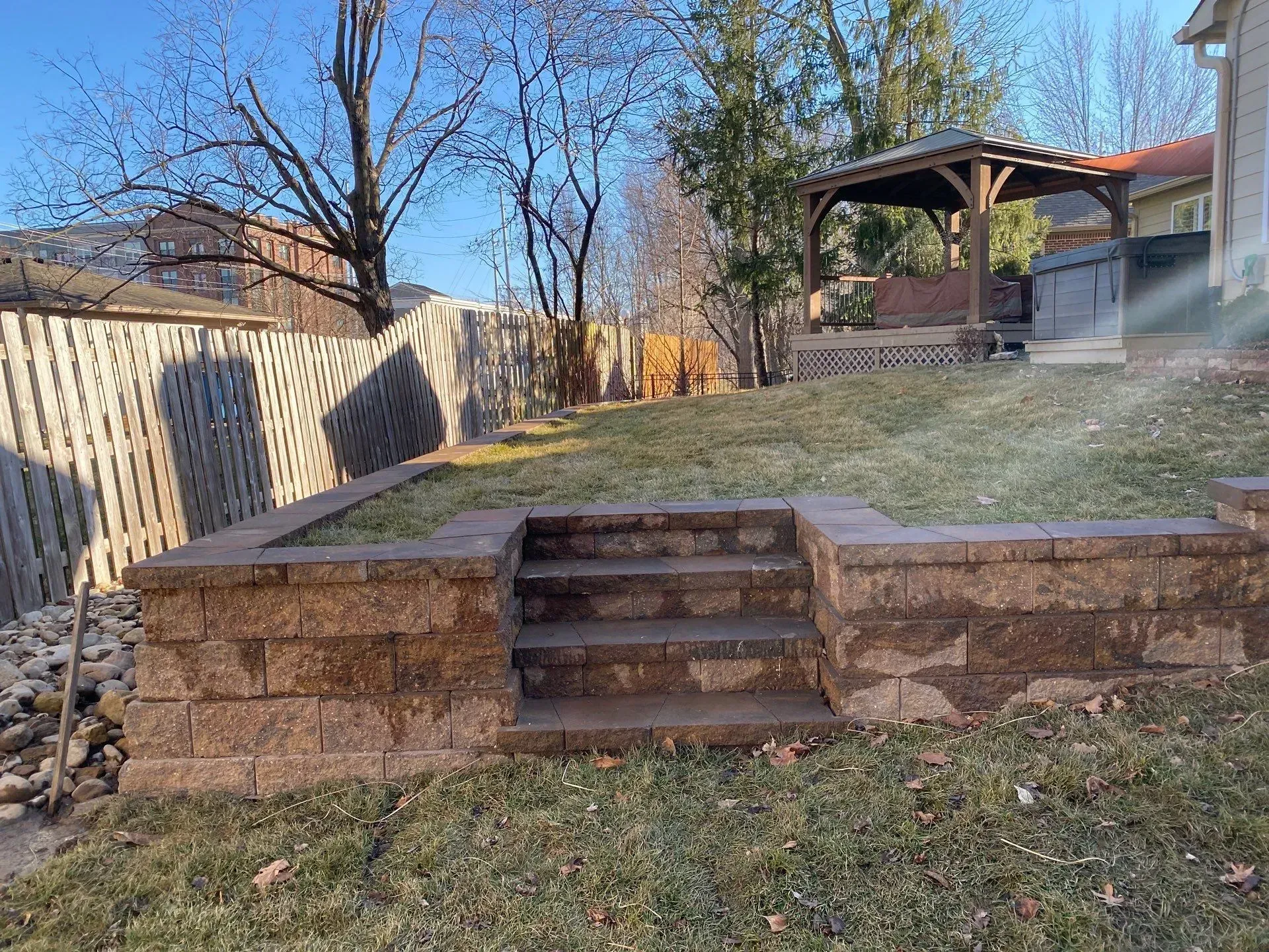 Backyard stone retaining wall with central steps leading to a raised lawn and gazebo