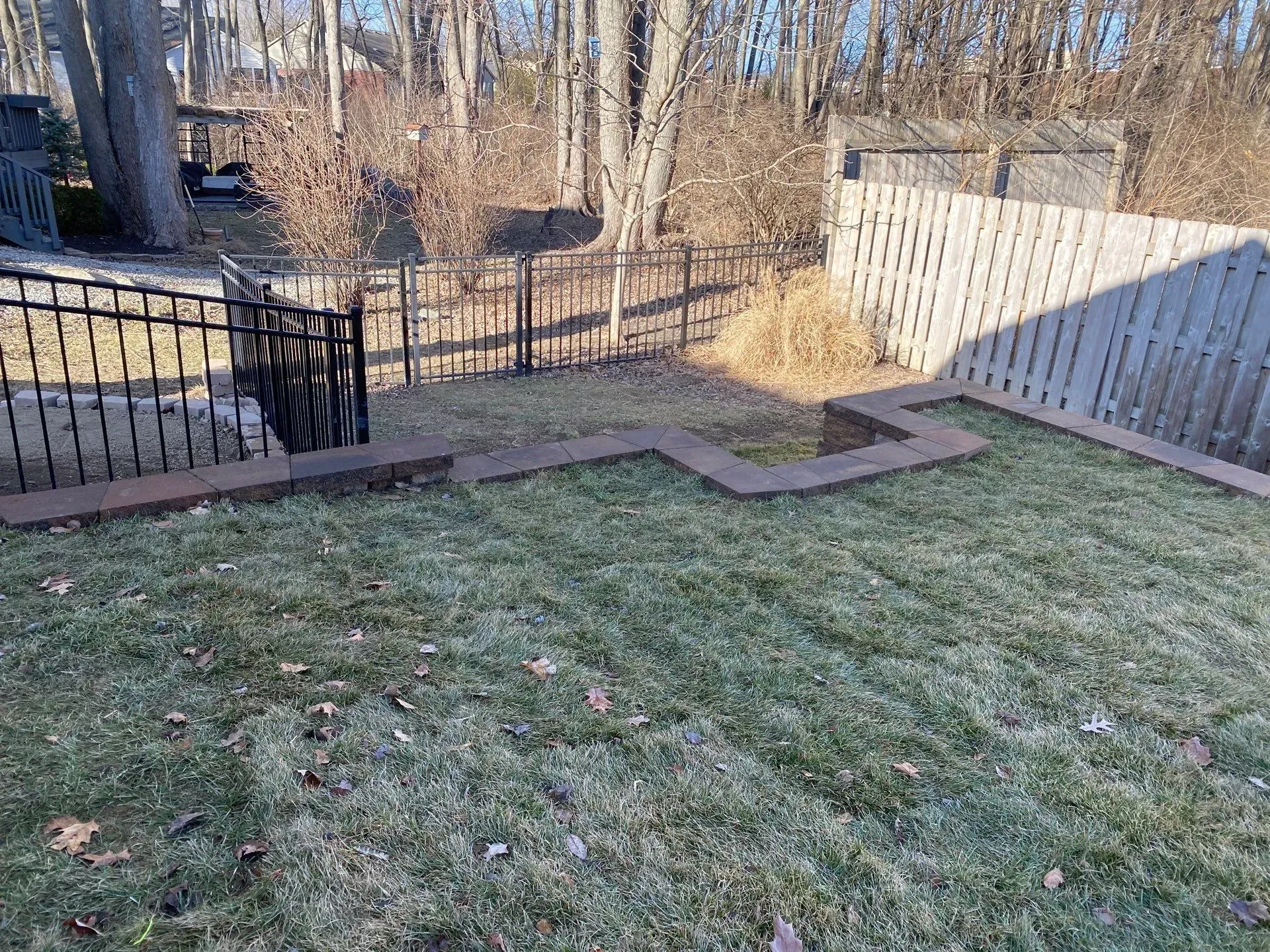Backyard with frosty grass, a patio, fence, and a small black cat near the gate
