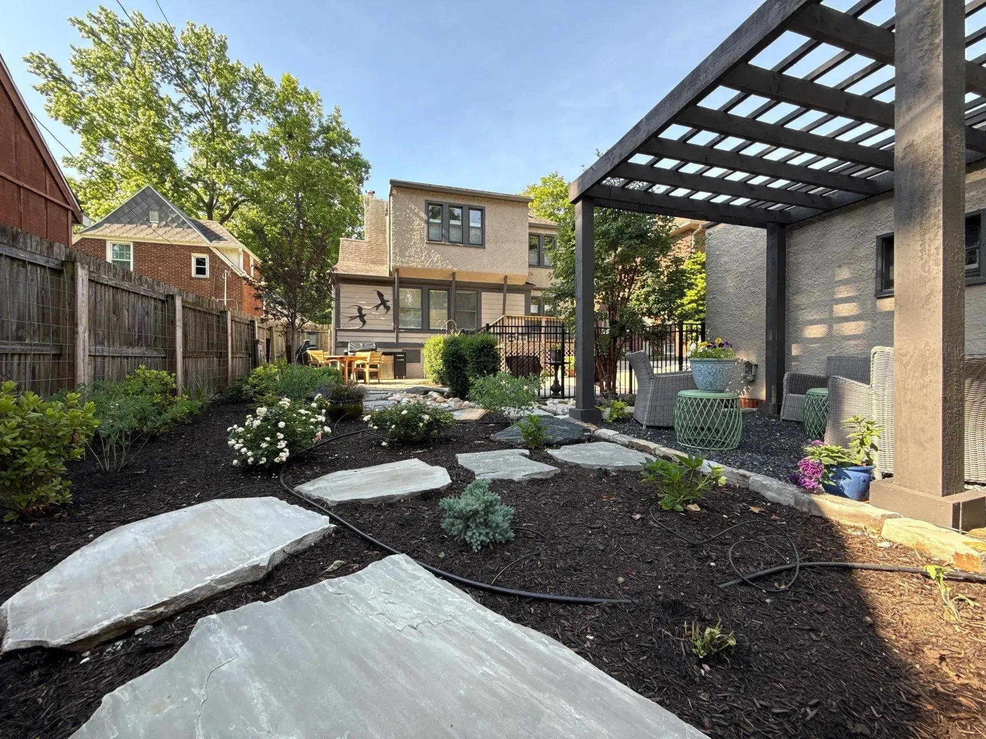 Modern backyard with stone path, dark mulch garden beds, pergola, and brick patio seating area