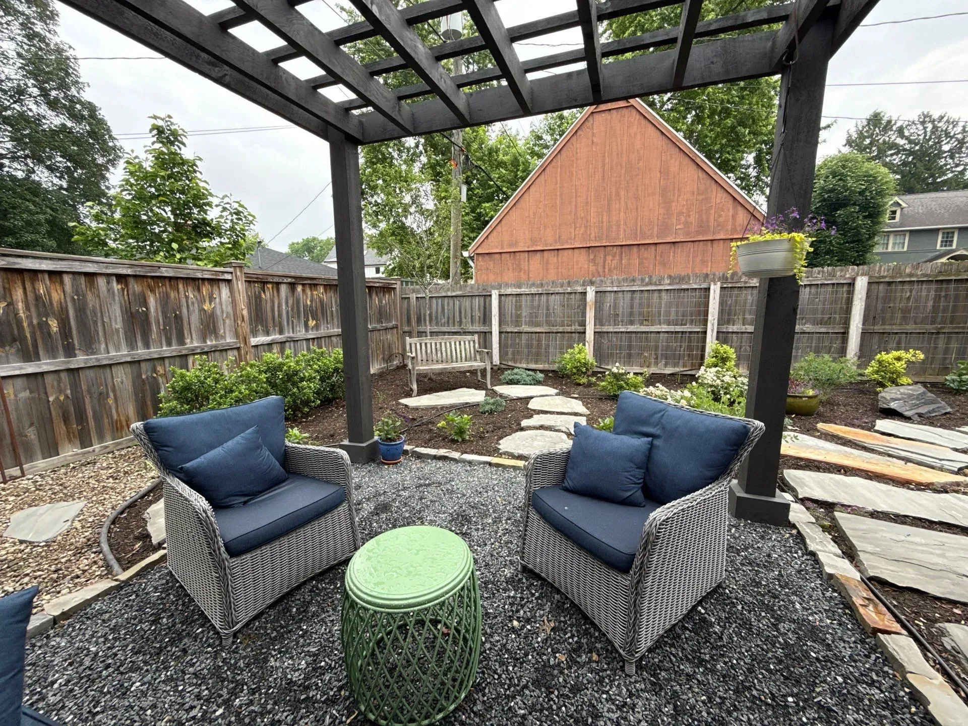 Covered patio with two blue chairs, a green table, and a landscaped backyard garden.