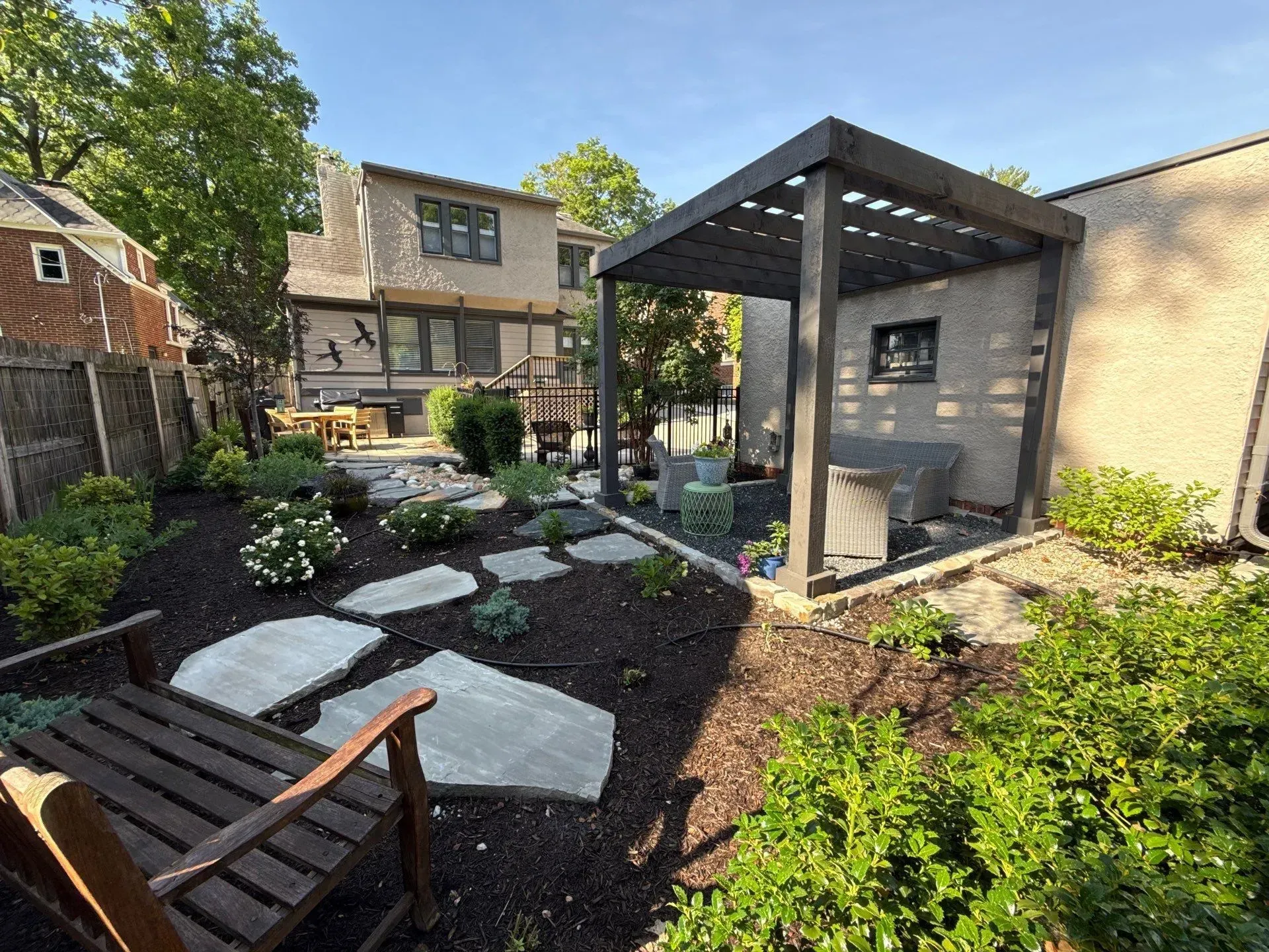 Modern backyard patio with pergola, lounge chairs, fire pit, and landscaping