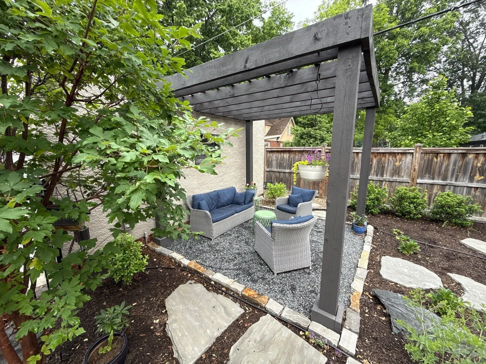 Backyard patio with pergola, blue seating, and gravel landscaping surrounded by greenery