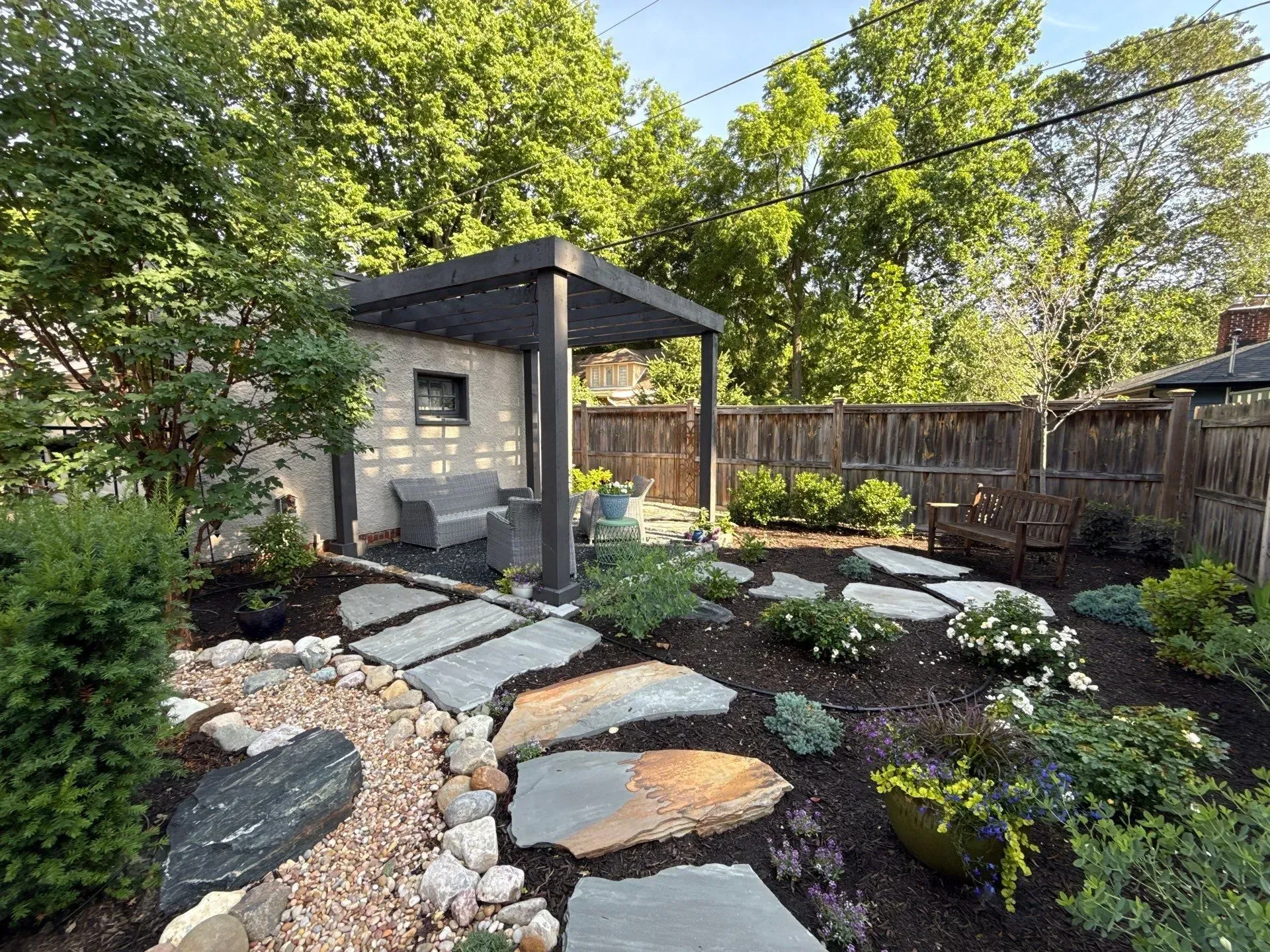 Landscaped backyard with stone path, gravel, pergola, and potted plants