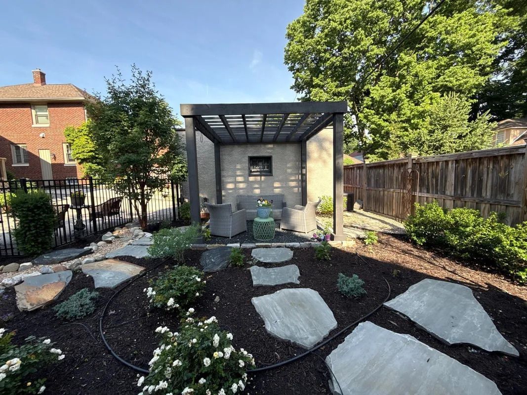 Backyard garden path with large stepping stones leading to a small stone shed under a slatted roof.