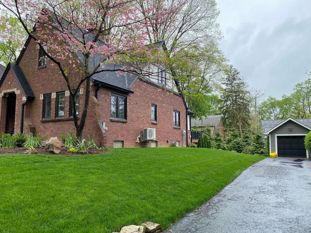 Brick house with pink-blossomed trees, green lawn, and a wet driveway leading to a garage.