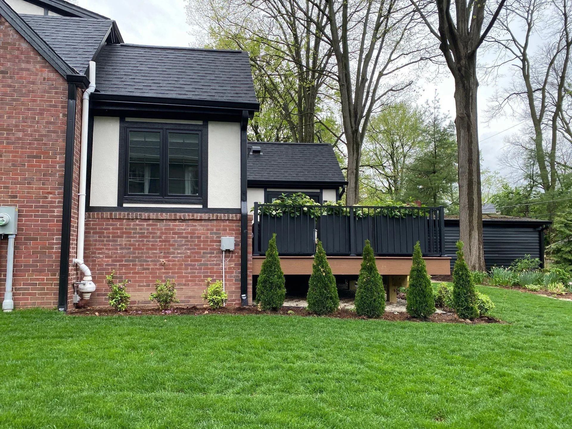 Brick house exterior with black-trimmed windows, green lawn, and young shrubs in front.