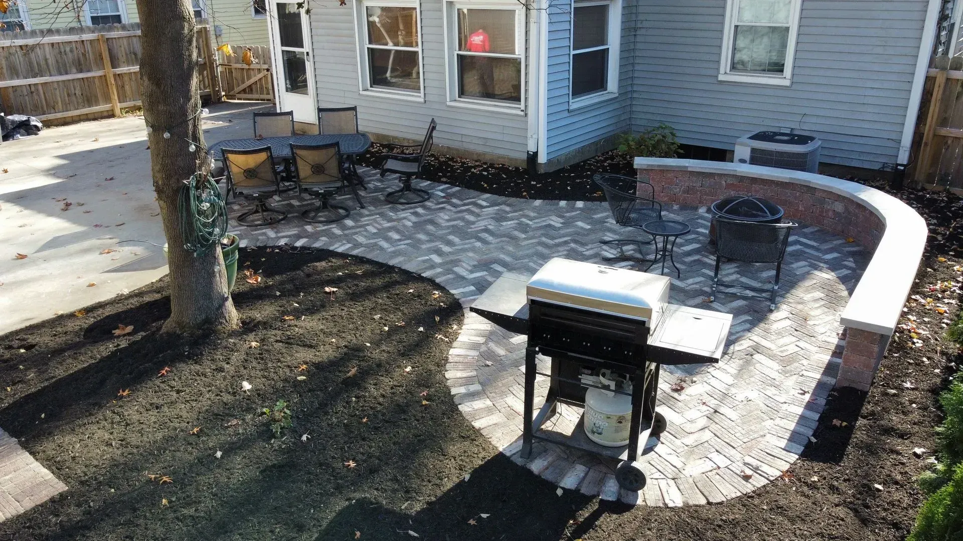 Backyard patio with grill, curved stone edging, and snow beside a house