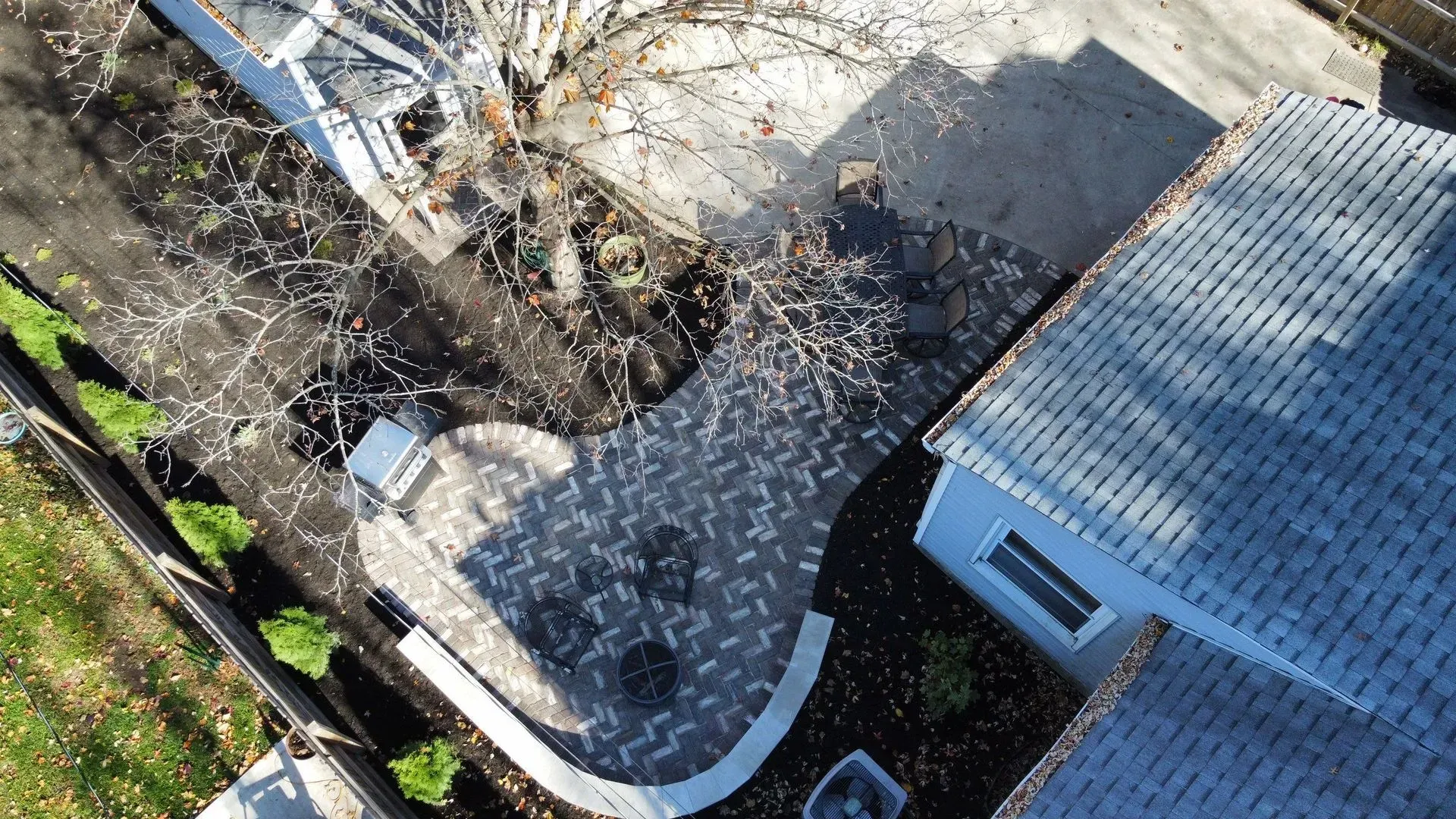 Aerial view of a small yard with paving stones, trees, and a gray-roofed building.