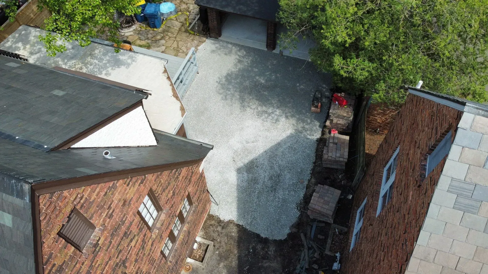 Aerial view of a gravel courtyard between brick buildings, with trees and parked bins along the edges