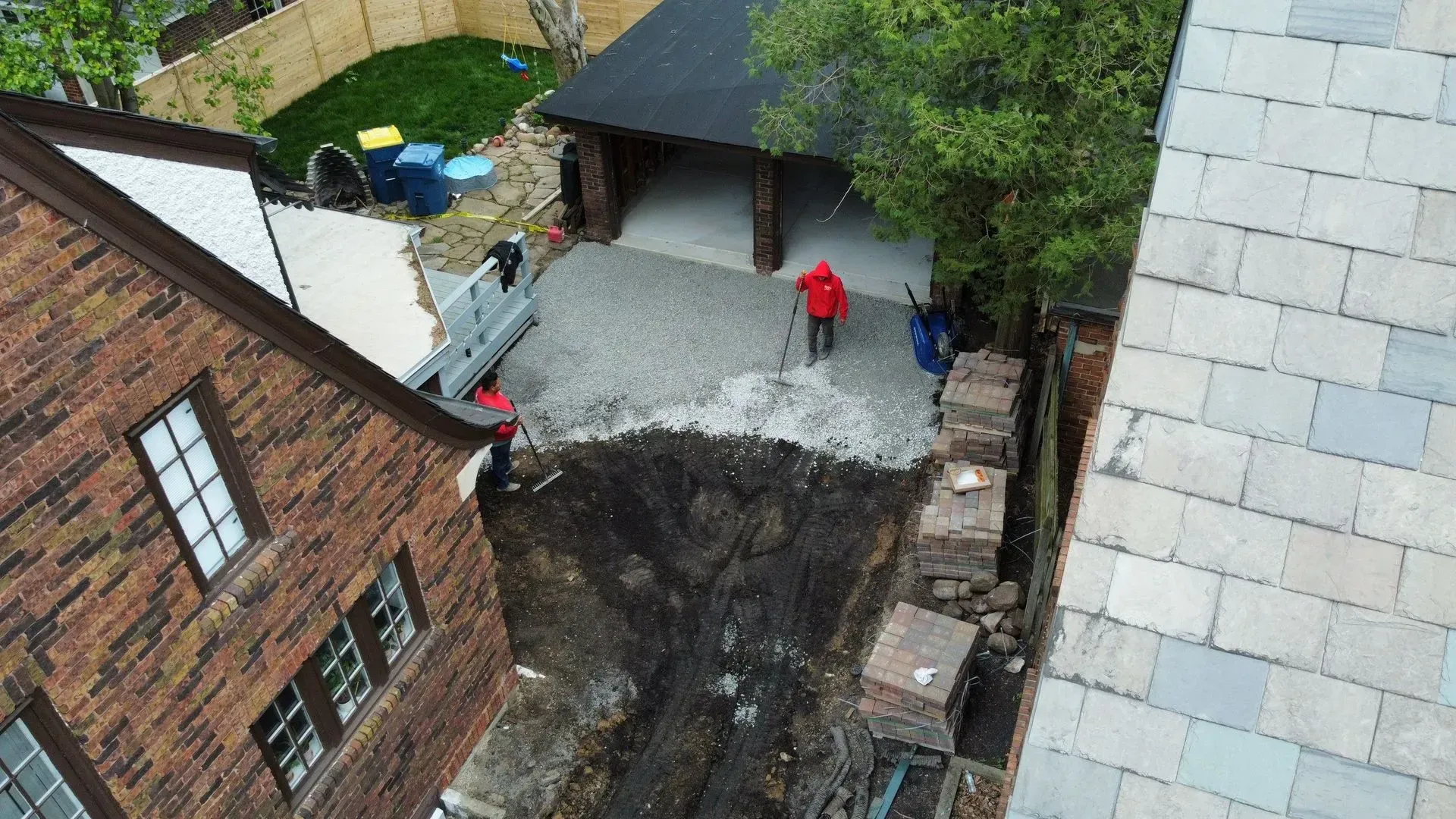 Overhead view of a courtyard with two people near a garage, brick buildings, and a driveway under construction