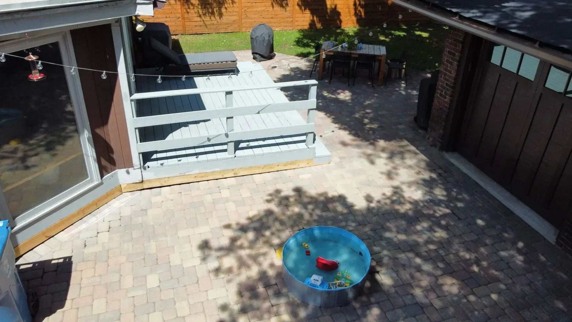Backyard patio with stone pavers, a white bench, and a blue glass fire pit table.