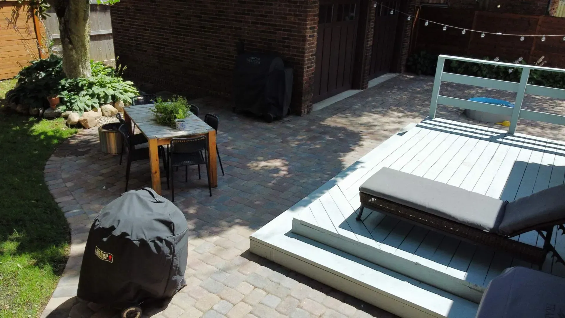 Sunny patio with outdoor chairs, table, potted plants, and a white lounge bed on a brick terrace.