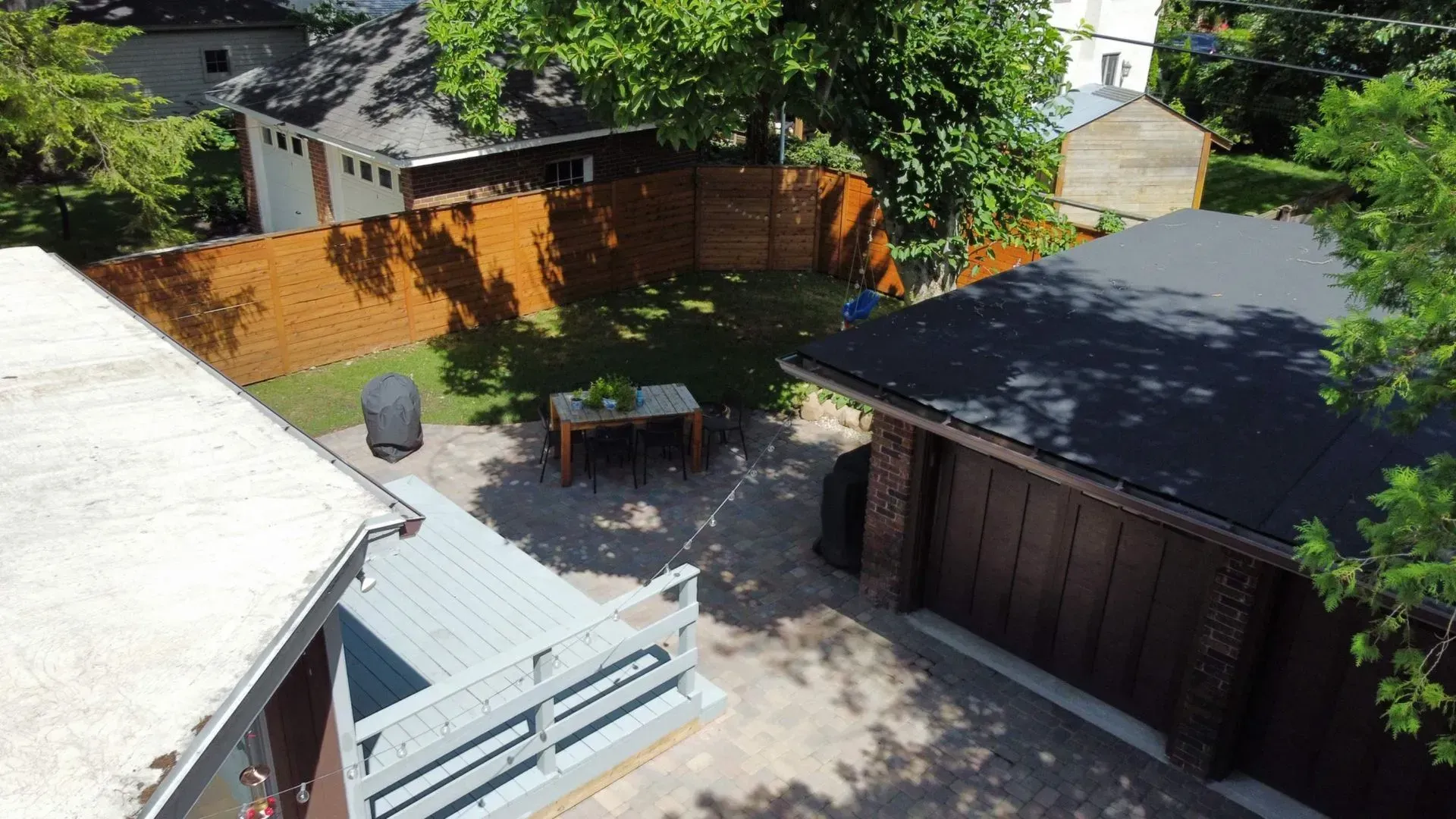 Backyard patio with tables, a grill, wooden fence, and a detached garage under bright sunlight