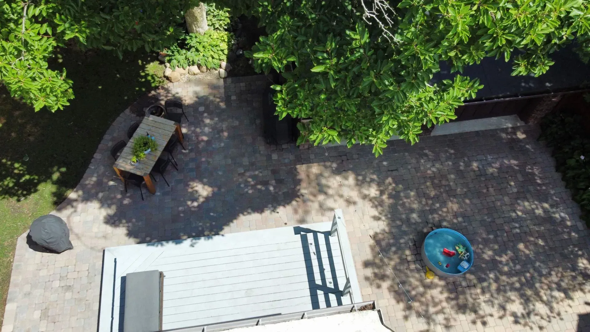 Overhead view of a shaded courtyard with picnic table, white deck, bench, and a blue kiddie pool.