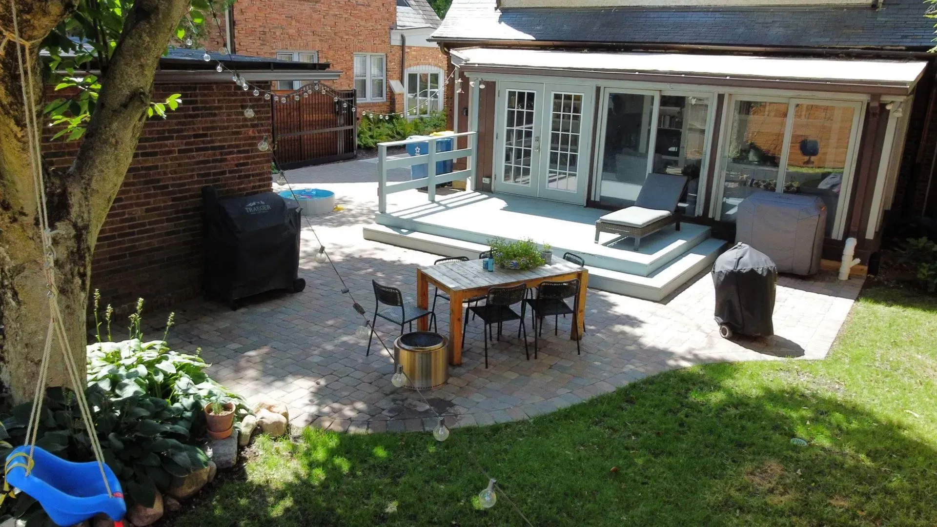 Backyard patio with outdoor dining table, chairs, grill, and a sunken hot tub beside a house