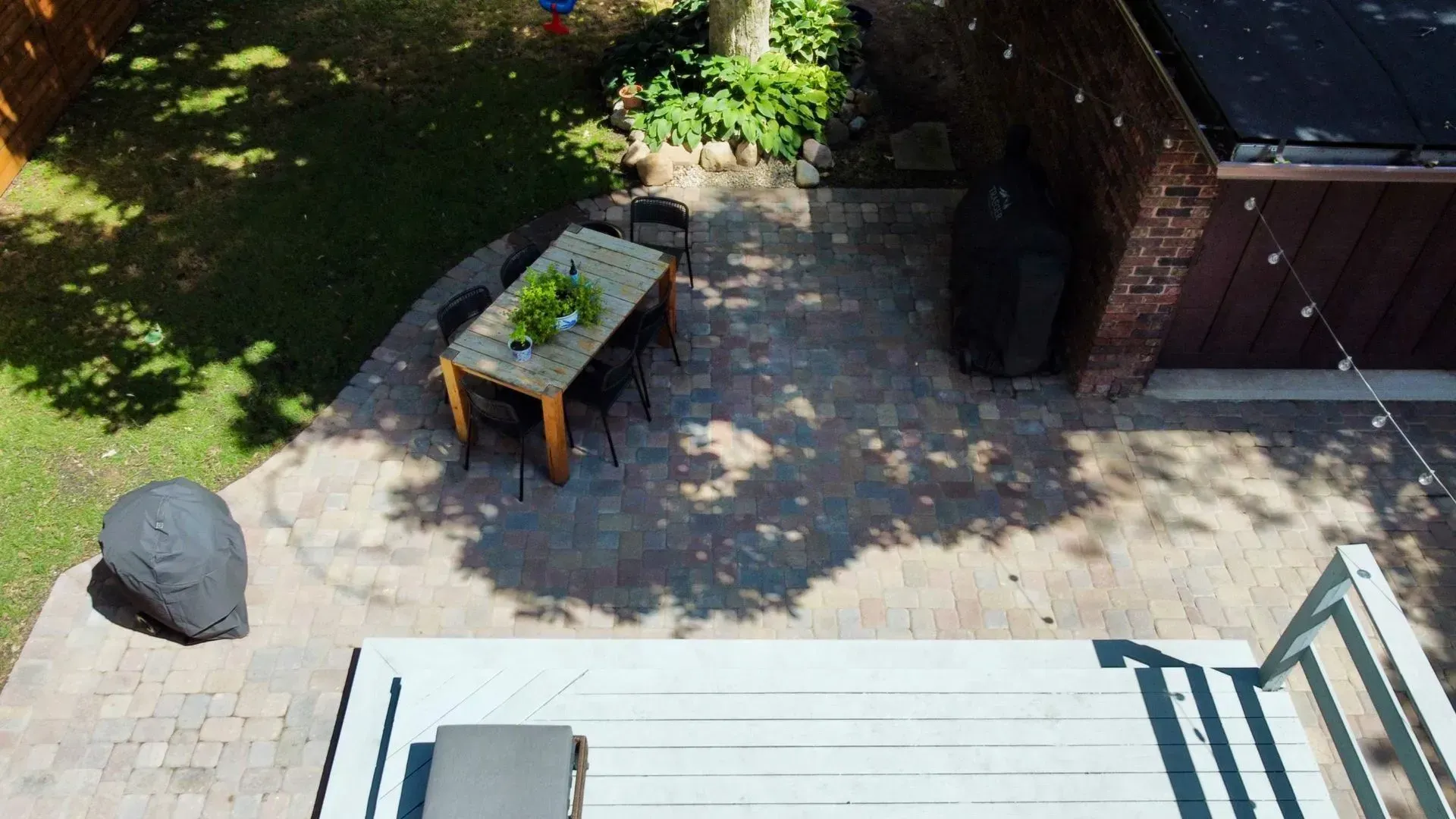 Backyard patio with a table, covered grill, brick wall, and sunlit deck stairs