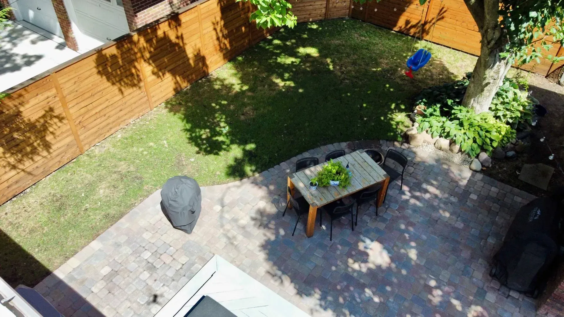 Backyard patio with a table, chair, fire pit, and lawn beside a wooden fence and tree shade