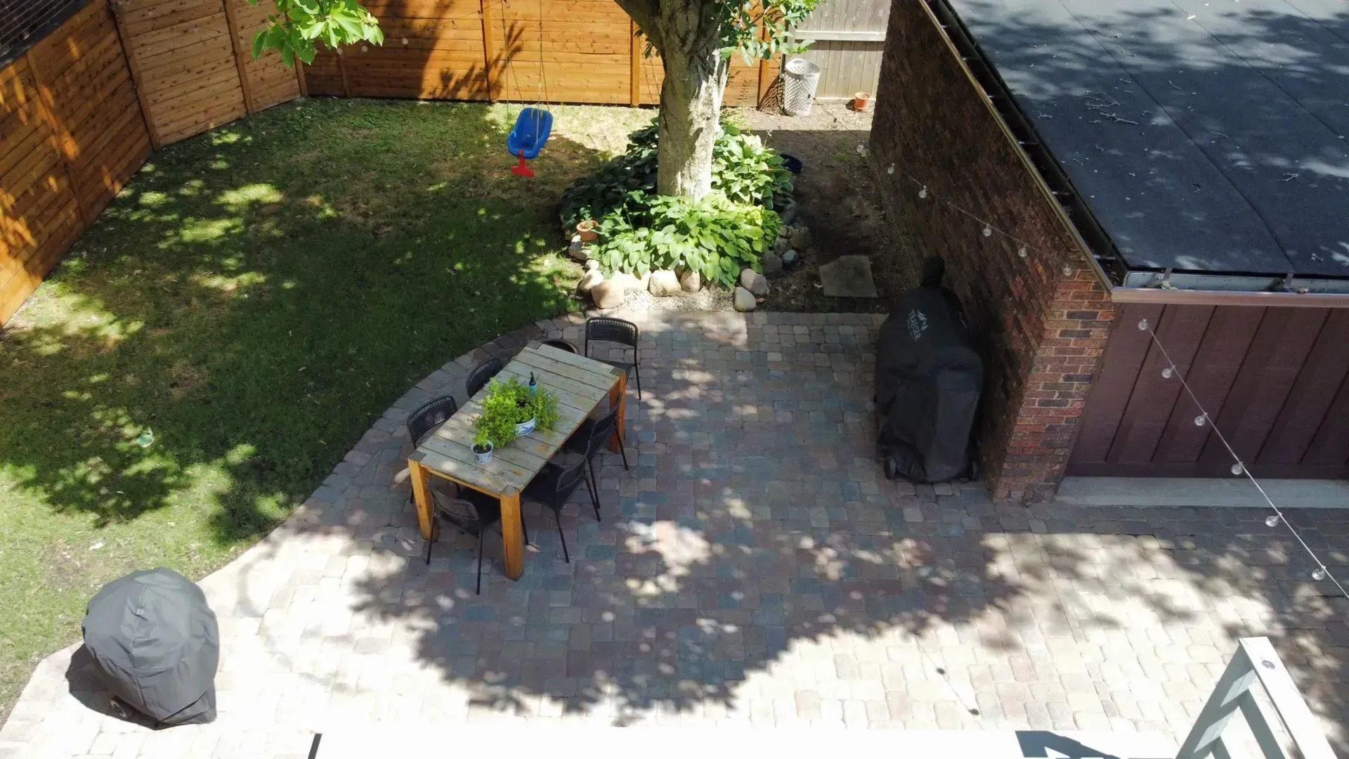 Backyard patio with table, grill, fenced lawn, and sunlight shadows