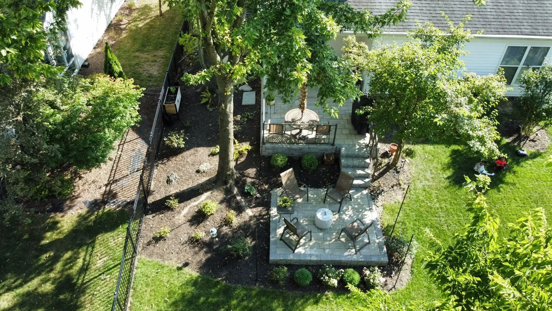 Aerial view of a backyard patio with outdoor tables, chairs, and surrounding trees and greenery