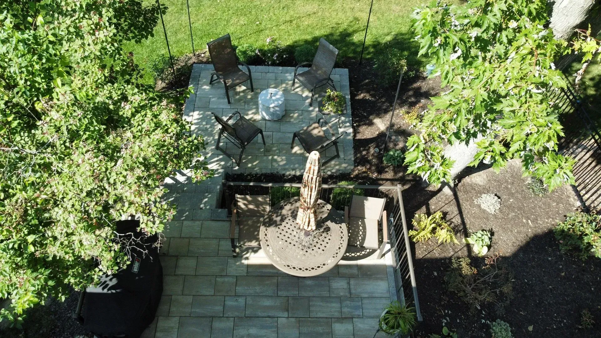Backyard patio with a round metal table and chairs under trees, seen from above.